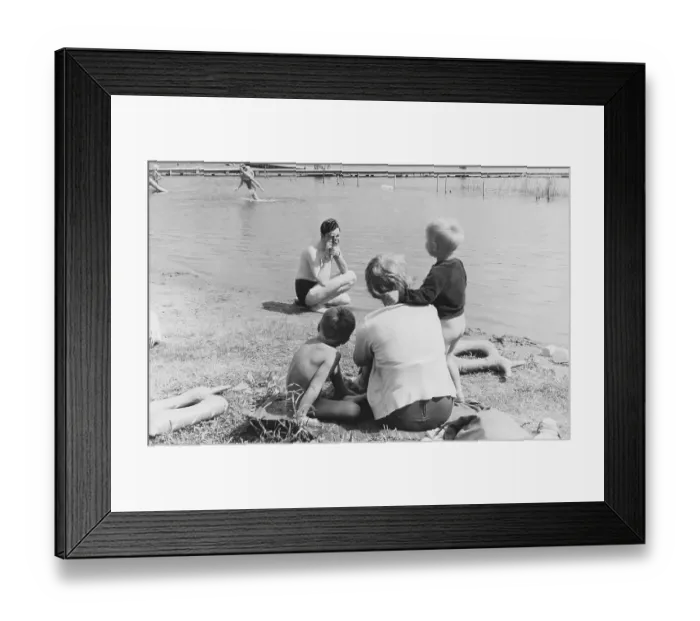 Framed Print : Family in the 1950s. A mother and her children sits on the beach while her husband is filming her with a amateur film camera. The film was then developed and shown on a film projector on a fold up screen. The film had no sound