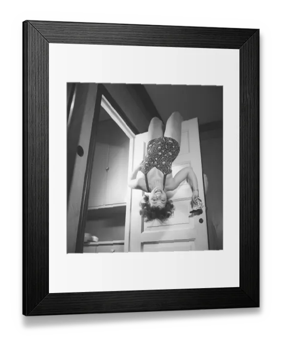 Framed Print : Woman in the 1940s. A young woman is proving to be both atletic and creative when hanging by her knees on an open door. She is dressed in a typical 1940s swimsuit. Sweden 1946 Kristoffersson ref M55-5