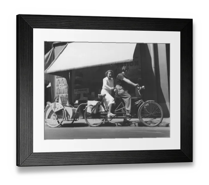 Framed Print : 1940s couple on a tandem bicycle. The young couple have their son in a bicycle carriage behind their bicycle. Sweden 1940s