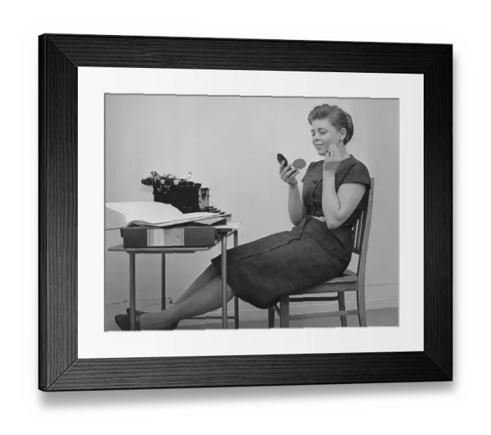 Framed Print : Office girl in the 1950s. A young girl at her typewriter is taking a break from work and is bettering her make up. Sweden 1955