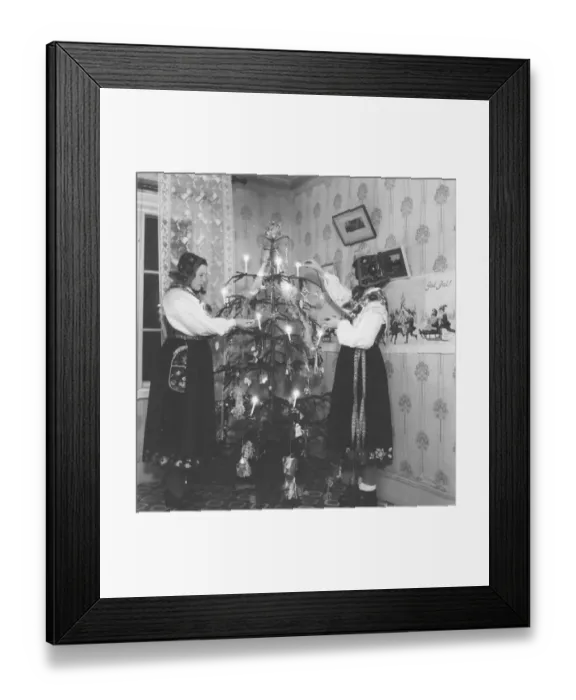 Framed Print : Christmas in the 1940s. Two young women in traditional swedish costumes are lighting the candles in the christmas tree