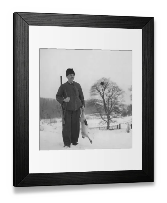 Framed Print : Hunter in the 1940s. A man is standing and holding a hare he has shot when hunting for the traditional christmas hare