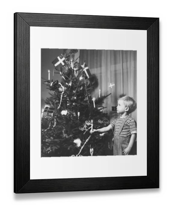 Framed Print : Christmas in the 1940s. A boy is standing by the decorated christmas tree