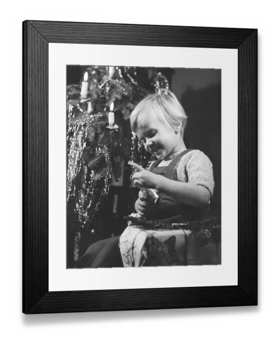 Framed Print : Christmas in the 1940s. A girl is opening her christmas present by the christmas tree