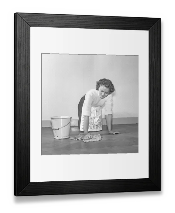 Framed Print : Cleaning the floor back then. A young woman is lying on the floor and use a scrubbing brush to get the floor clean