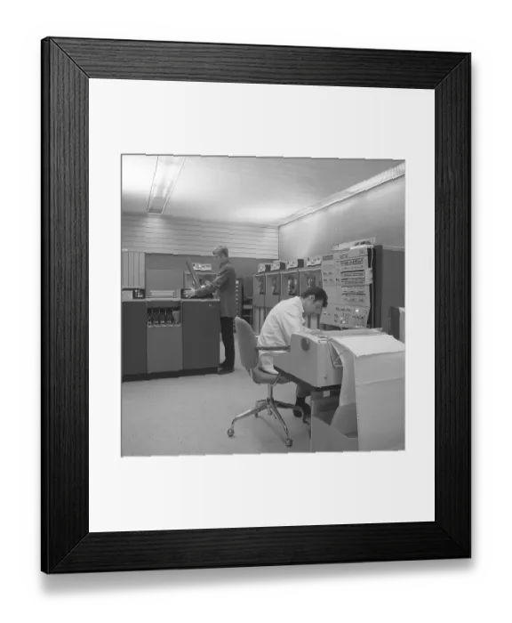 Framed Print : In the 1960s. Interior of a room with computers and people on the job of handling them and register and reading information. A sign above the mainframe computer says IBM 360 Framed Print : In the 1960s. Interior of a room with computers and people on the job of handling them and register and reading information. A sign above the mainframe computer says IBM 360