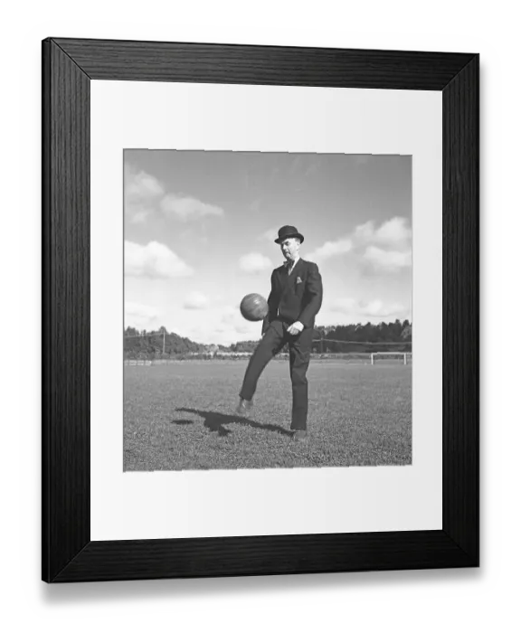 Framed Print : 1940s soccer player. A gentleman dressed in a suit and a bowler hat is kicking a football in the air