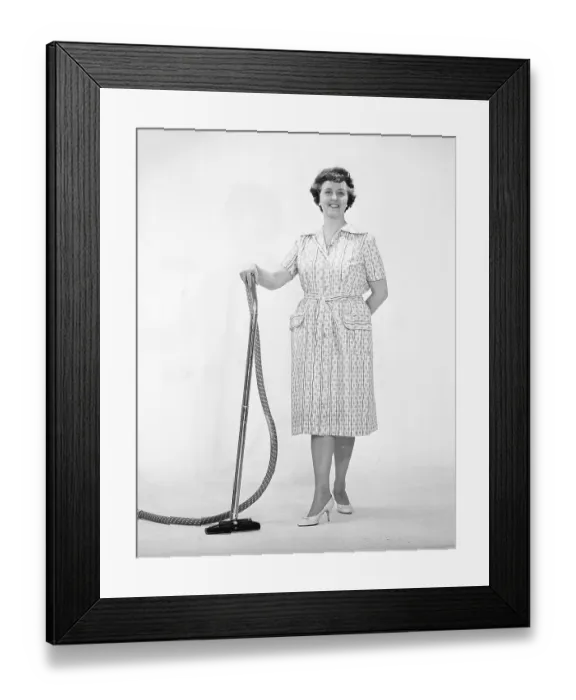 Framed Print : Cleaning day in the 1960s. A woman is standing holding a vacuum cleaner