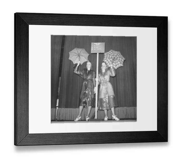 Framed Print : 1940s women in raincoats. Two young woman dressed in raincoats of plastic material is showing them with umbrellas