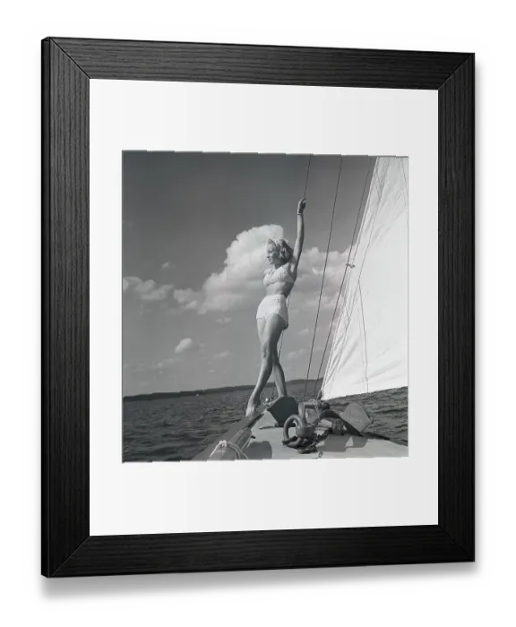Framed Print : 1940s sailing boat. A young woman is aboard a fashionable sailing boat and is standing on deck when it cruises forward with wind in the sails. She is wearing a typical 1940s two piece bathing suit. Sweden 1946 Photo Kristoffersson ref AC101-4