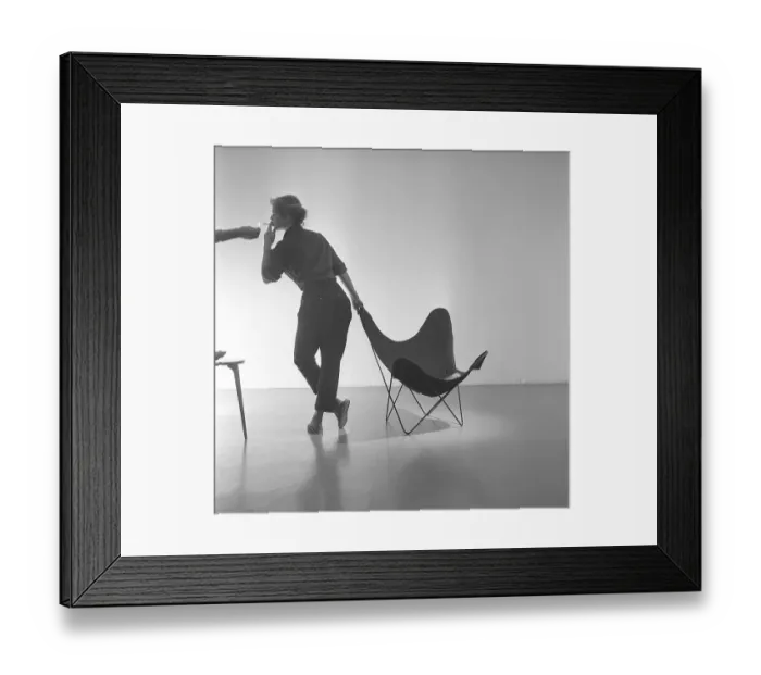 Framed Print : Home decor of the 1950s. A young woman is standing beside the popular Butterfly chair Framed Print : Home decor of the 1950s. A young woman is standing beside the popular Butterfly chair