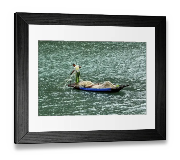 Framed Print : A fisherman pulls a large net from a small boat onto the water