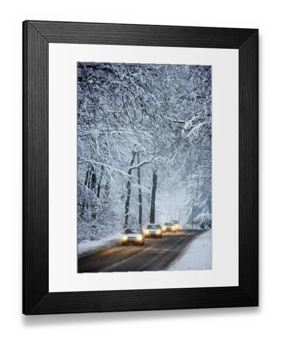 Framed Print : Driving in winter, vehicles on a cleared road in a snow-covered forest with falling snow