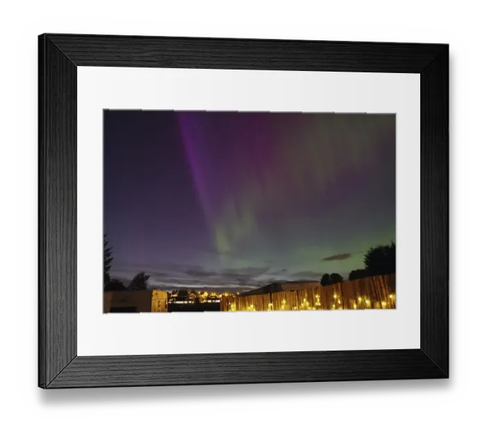 Framed Print : Northern Lights in the night sky above an illuminated fence and a campsite