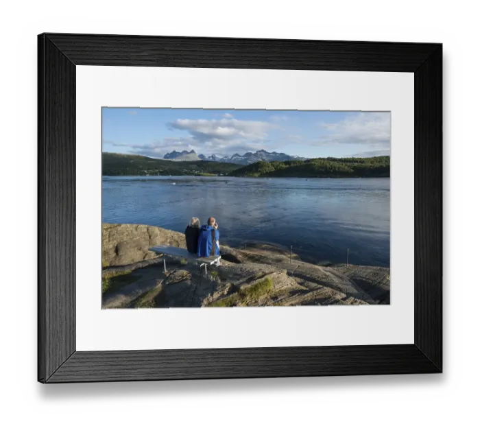 Framed Print : Couple sitting on a bench looking out to the tidal Saltstraumen strait in the evening light