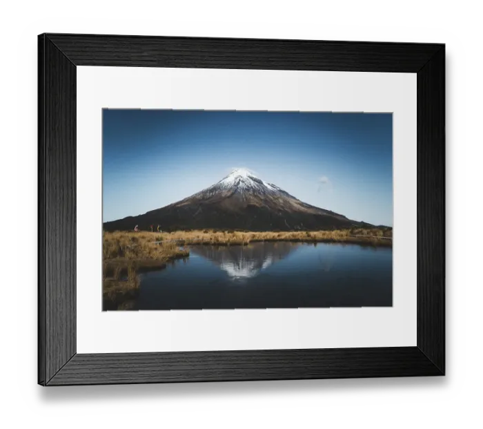 Framed Print : A snow-capped mountain is reflected in a still lake while people walk along the shore