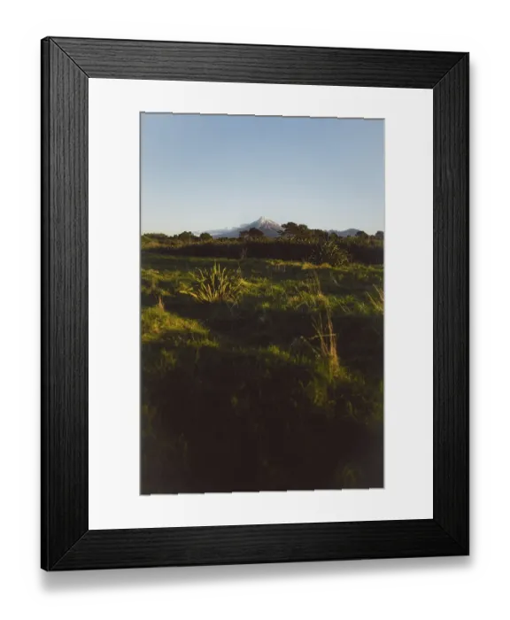Framed Print : A green hilly landscape under a clear blue sky with a mountain peak in the background creating a peaceful atmosphere