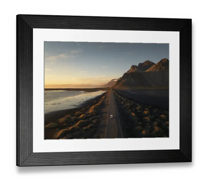 Framed Print : A lone car travels down a long dirt road flanked by dramatic mountainous terrain at sunset