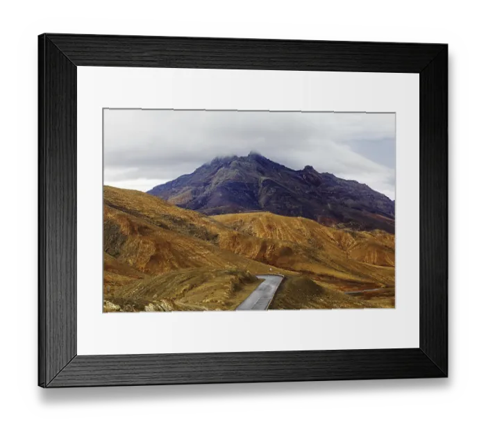 Framed Print : A winding road leads through a mountainous landscape under a cloudy sky