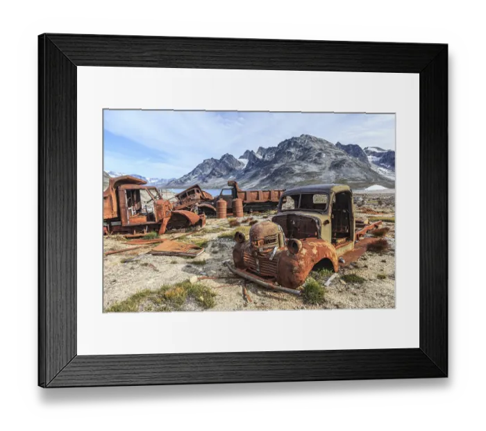 Framed Print : Rusty cars and oil drums in front of steep mountains