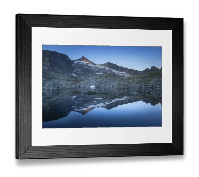 Framed Print : Reflection of snow-covered mountains on a calm water surface under a blue sky at sunrise