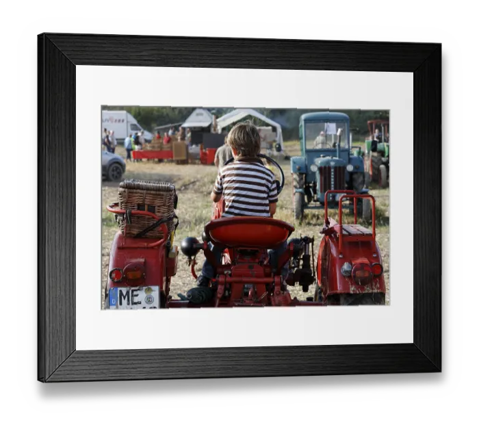 Framed Print : Small boy sitting at the wheel of a vintage tractor