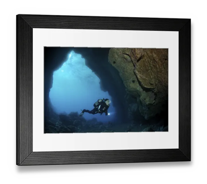 Framed Print : Diver with torch diving in a rock cave