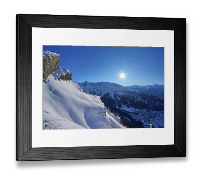 Framed Print : Mountain peak with snow-covered rocks under a clear blue sky with sun