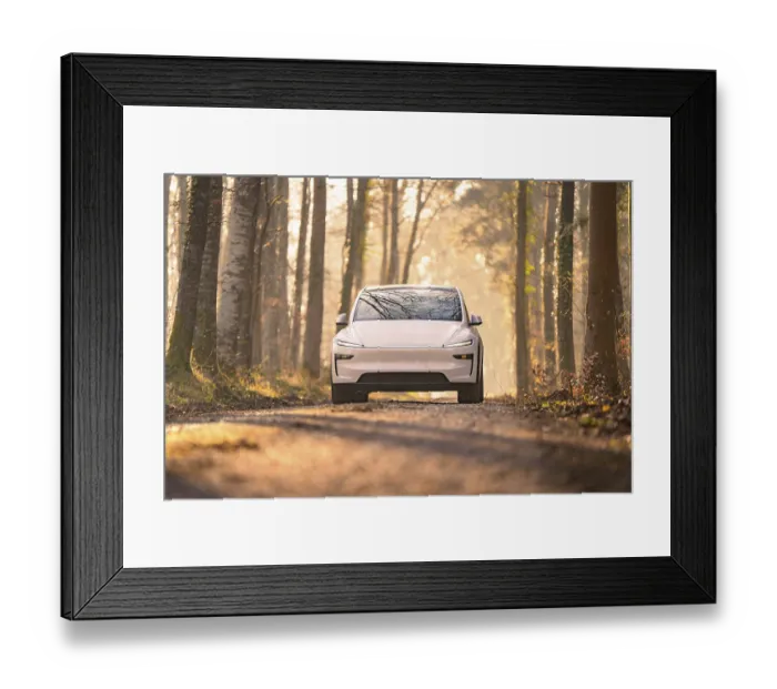 Framed Print : White electric car driving on a tree-lined forest path in soft sunlight