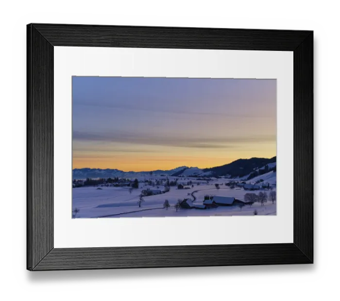 Framed Print : Snowy landscape at sunrise with mountains and farms