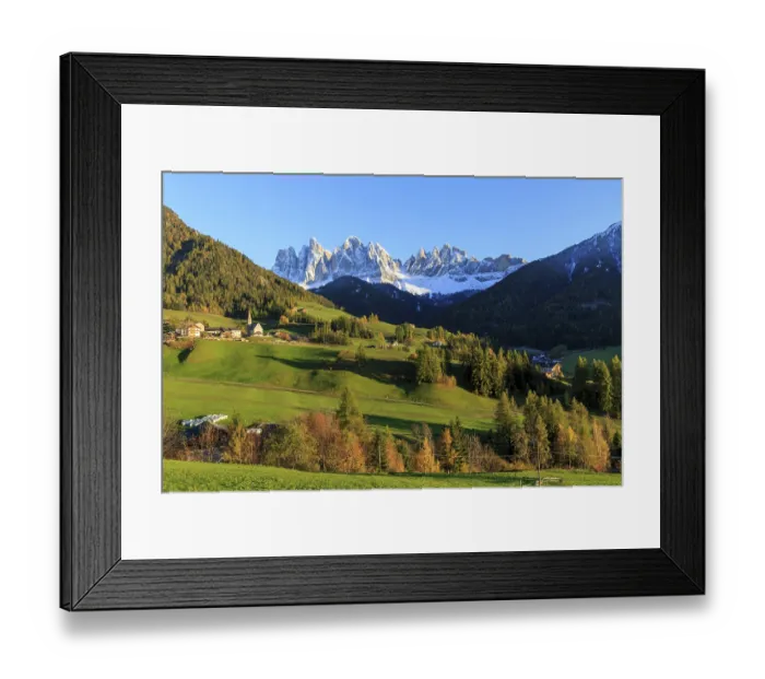 Framed Print : Sunlit village in a valley below a snow-covered mountain range