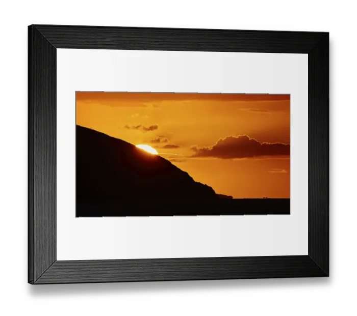 Framed Print : Soft orange light of the sun behind a mountain