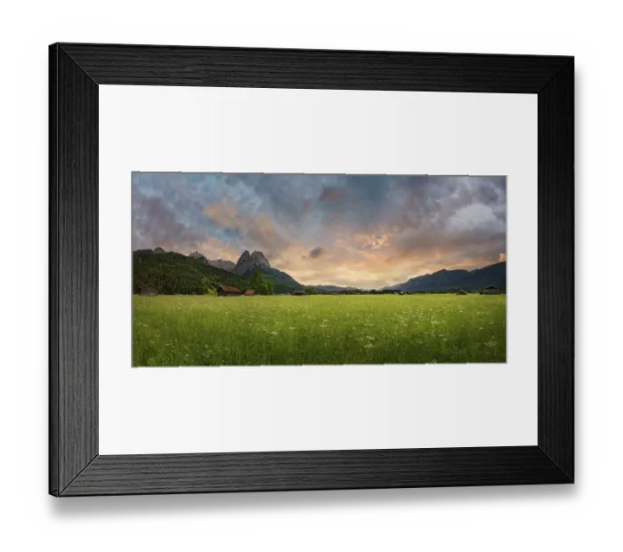 Framed Print : Panoramic view of a green meadow in front of imposing mountains under a cloudy evening sky Framed Print : Panoramic view of a green meadow in front of imposing mountains under a cloudy evening sky