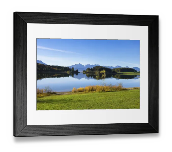 Framed Print : A calm lake reflects the surrounding mountains and forests under a clear sky