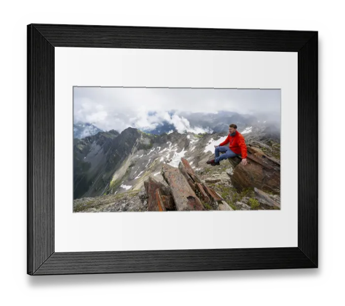 Framed Print : Mountaineer sitting on a rock, cloudy mountain landscape at the summit of Lasoerling