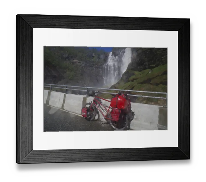 Framed Print : A packed bicycle stands on a road in front of an impressive waterfall in a mountainous landscape