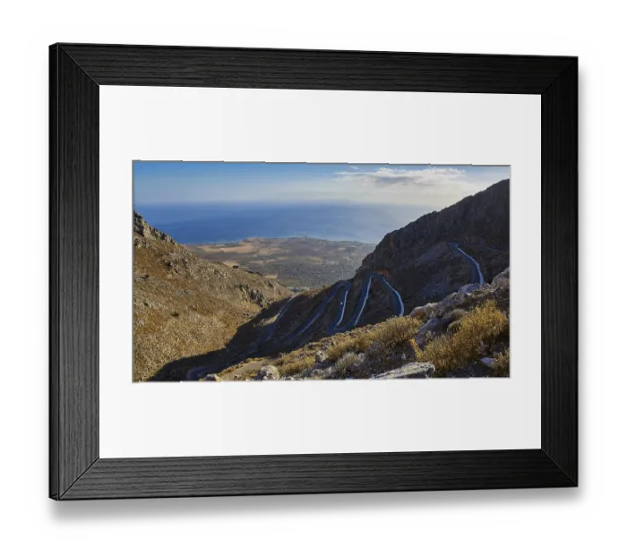 Framed Print : Serpentine road winds through a dry mountainous landscape down to the sea