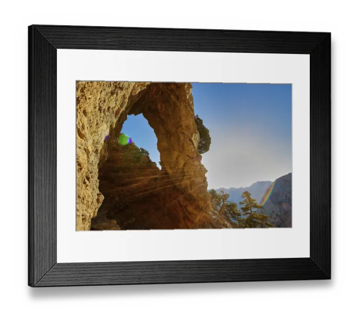Framed Print : A rocky arch with sunbeams, surrounded by trees and mountains under a clear sky