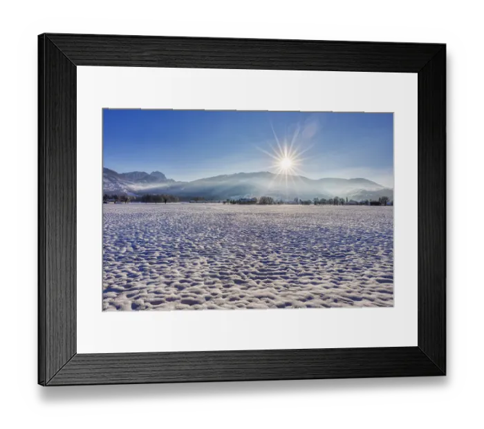 Framed Print : Winter landscape with snow-covered field and rising sun against a mountain backdrop Framed Print : Winter landscape with snow-covered field and rising sun against a mountain backdrop