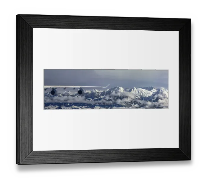 Framed Print : An aeroplane flies over a snow-covered mountain landscape and misty forests