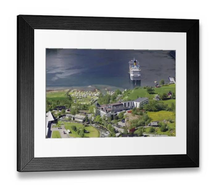 Framed Print : A large cruise ship is moored on a shore with many buildings and green meadows and trees