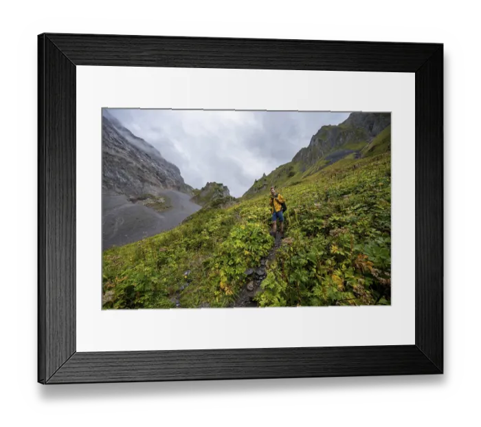 Framed Print : A mountaineer on a path surrounded by green vegetation and cloudy sky