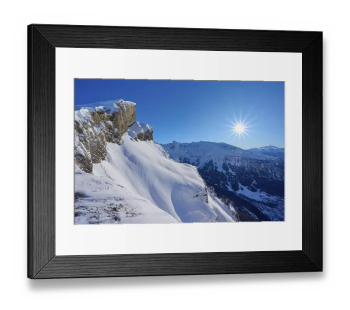 Framed Print : Mountain peak with snow-covered rocks under a clear blue sky with sun