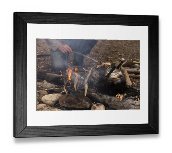 Framed Print : Coffee kettle on the campfire, behind it the legs of a person kneeling at the campfire Framed Print : Coffee kettle on the campfire, behind it the legs of a person kneeling at the campfire