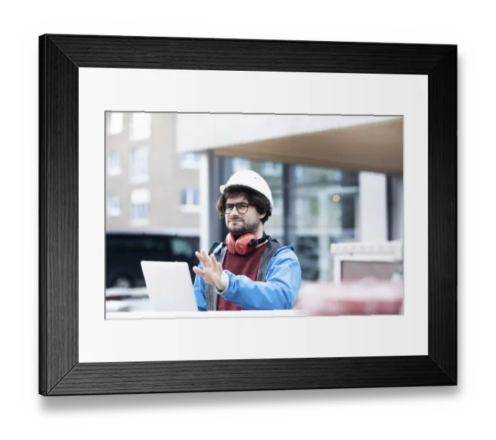 Framed Print : Young engineer with helmet and hearing protection checks outside work with laptop