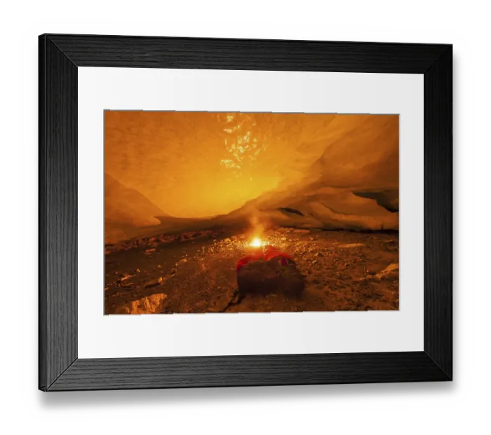 Framed Print : A glowing fire in a cave with a sleeping bag lying next to it creates an atmospheric scene