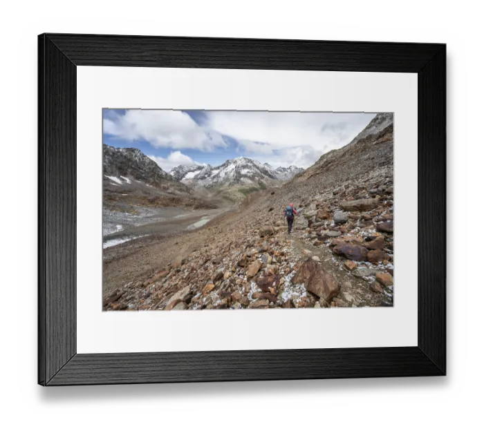 Framed Print : Mountaineer on hiking trail in steep rocky mountain landscape with fresh snow in summer