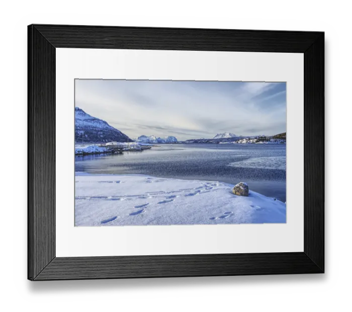 Framed Print : Footprints in the snow on the beach with a view of the sea and mountains under a blue sky