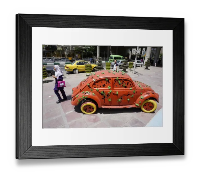 Framed Print : A woman walks past a Volkswagen Beetle art object on the pavement in Tehran