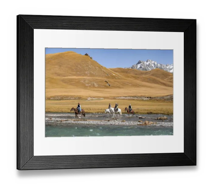 Framed Print : Riders riding through river in front of mountain landscape with yellow meadows Framed Print : Riders riding through river in front of mountain landscape with yellow meadows